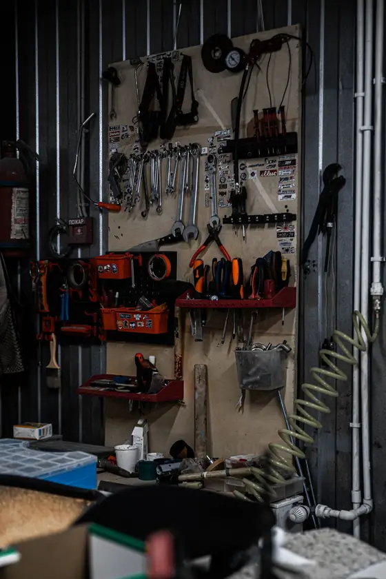 A garage workshop wall with tools and equipment hung on a board and shelves, in low light.