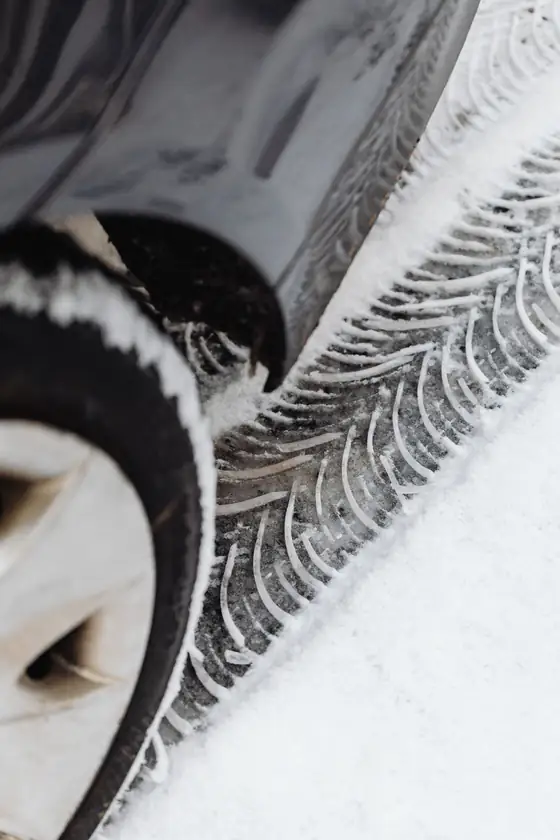 A car tire with a deep winter tread sitting in fresh snow, with tire tracks beside it.
